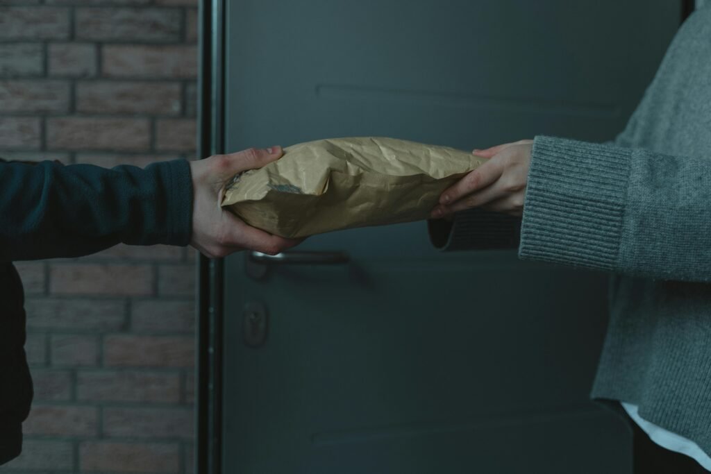 Close-up of hands exchanging a package at a doorway, symbolizing home delivery service.